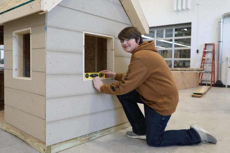 A student checks the level on the window of a small building inside the career and technical education shop.